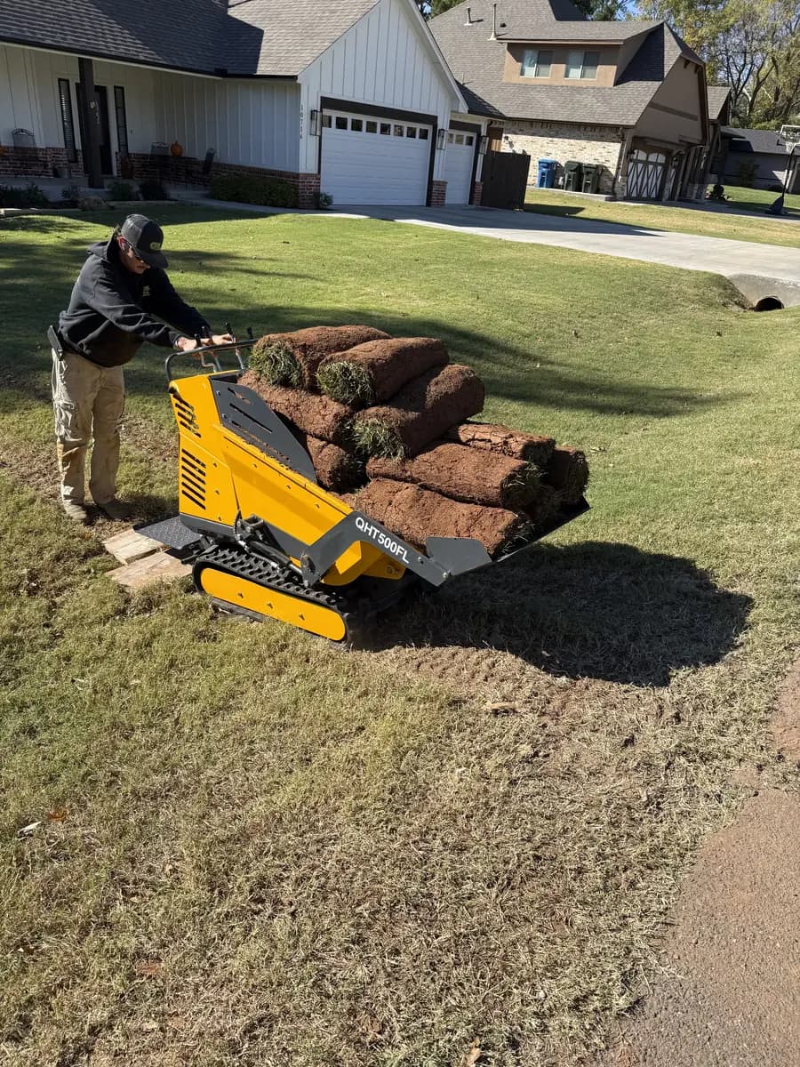 Greenline crew member operating a tracked carrier loaded with rolls of sod on a front lawn
