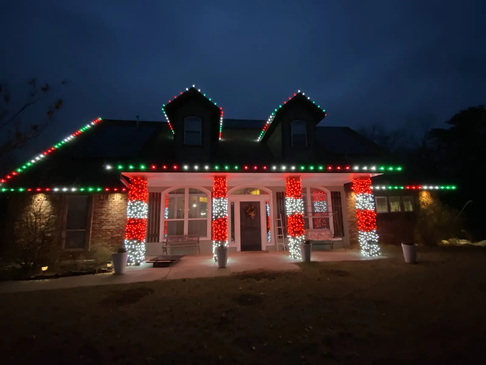 Residential home decorated with red, green, and white roofline lights and wrapped porch columns