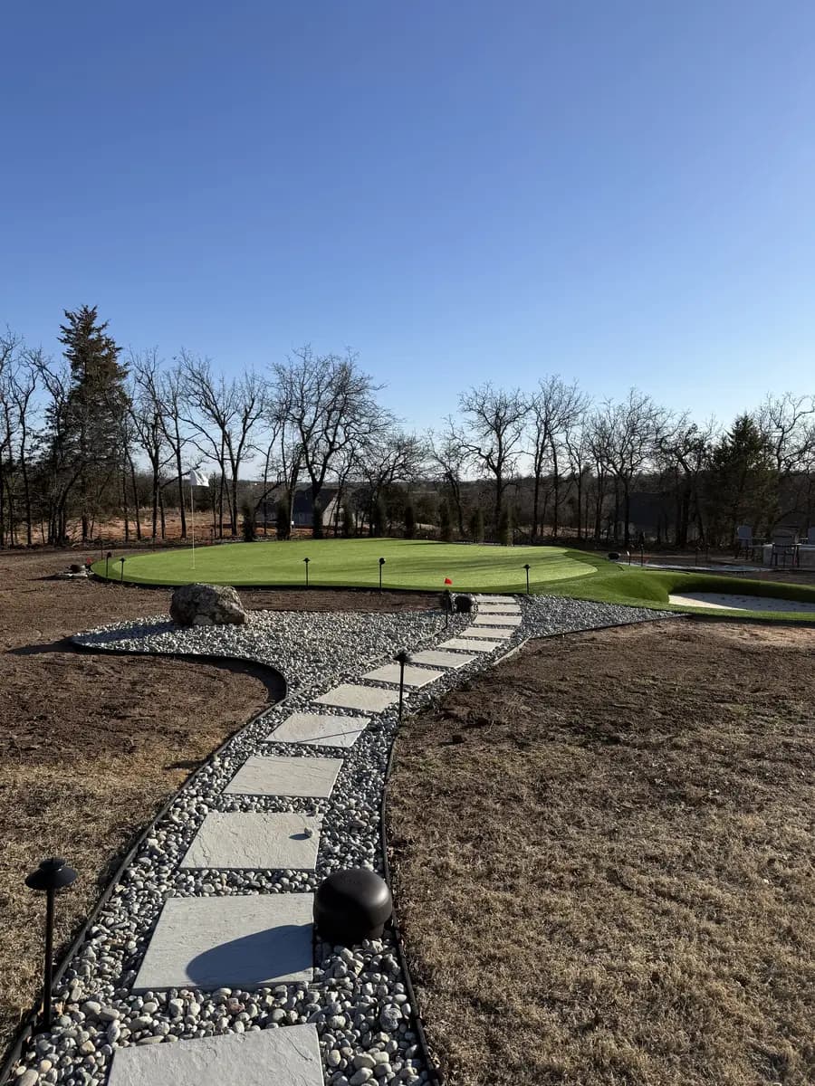 Square stepping stones set in river rock leading toward a landscaped backyard putting green
