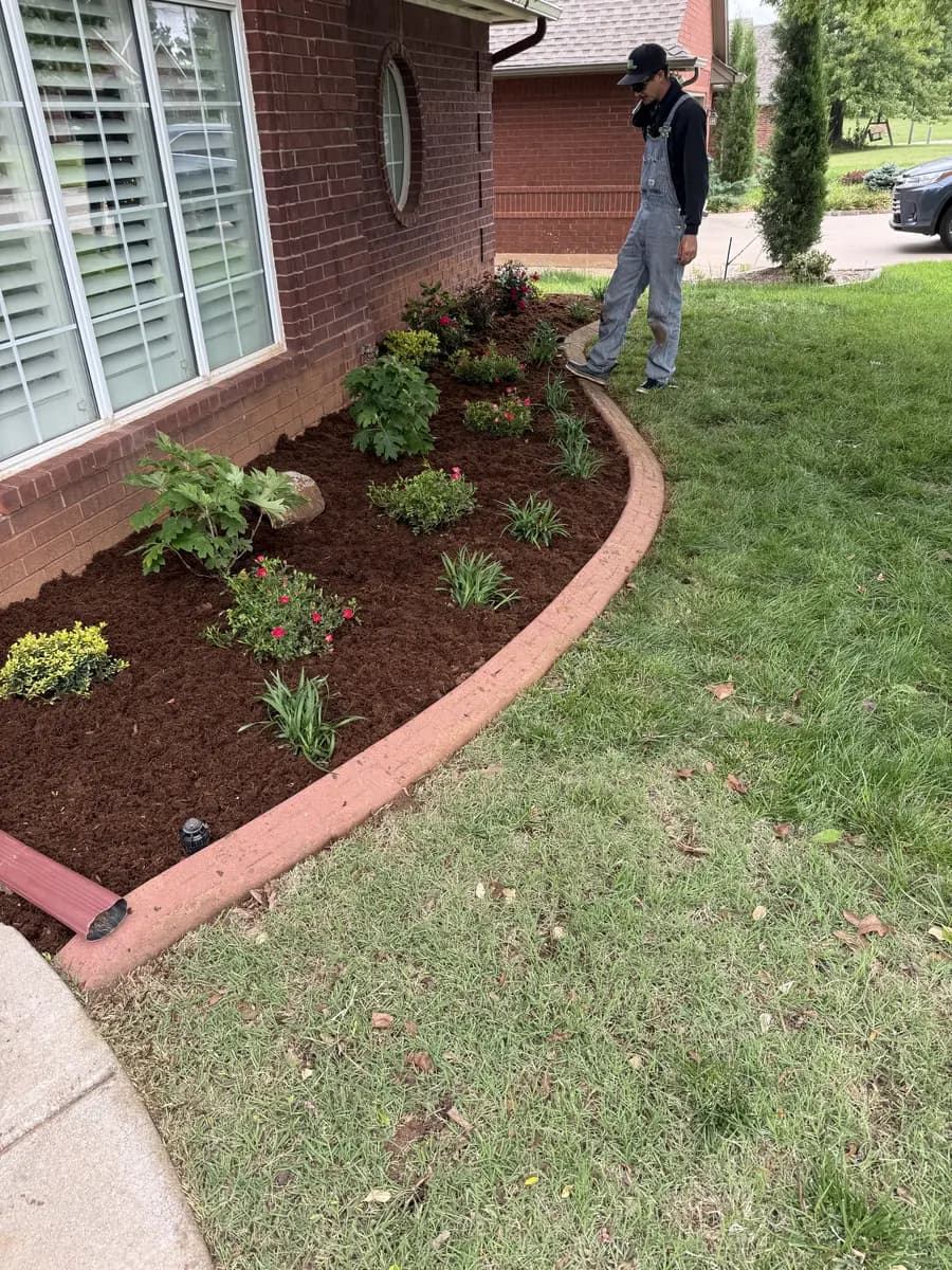 Greenline crew member inspecting a curved residential bed with new plants and fresh mulch
