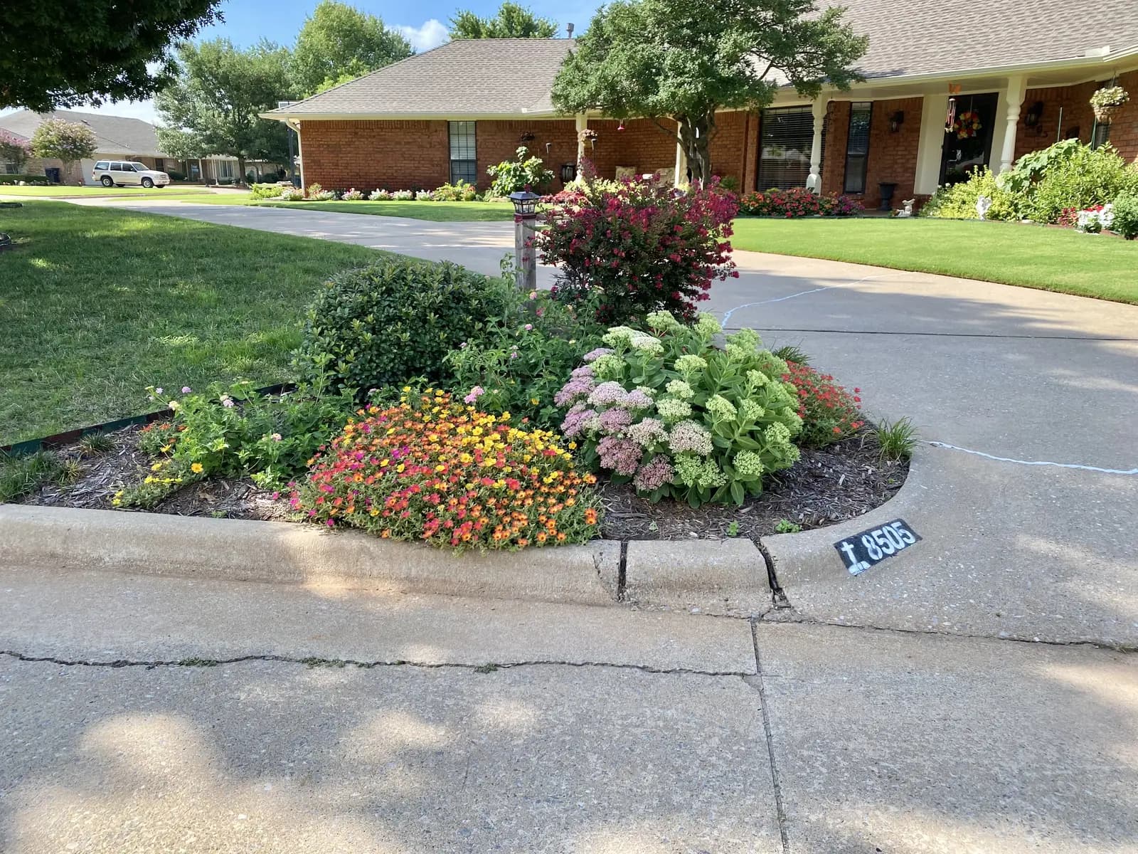 Mature flowering landscape bed beside the driveway of a red-brick Oklahoma home