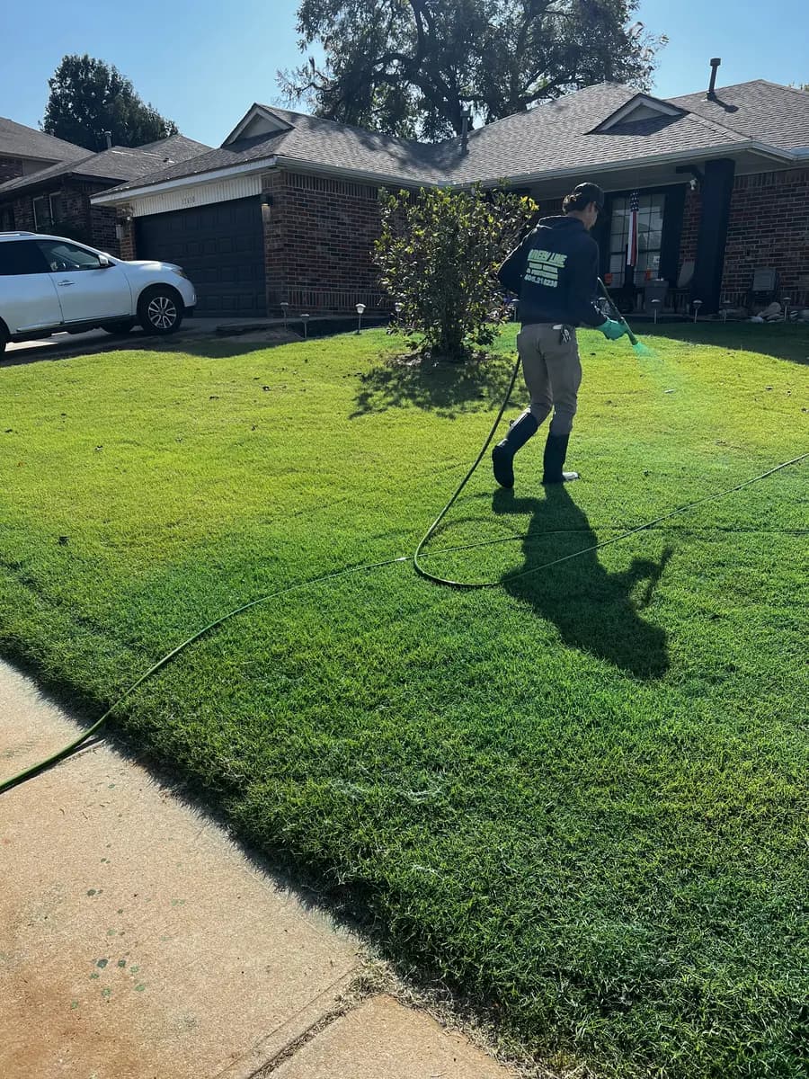 Greenline technician spraying green-marked liquid treatment across a residential front lawn